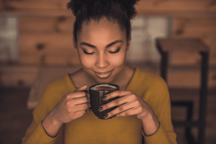 woman wearing yellow shirt smiles while inhaling cup of coffee